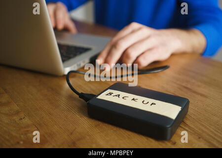 Midsection of man using laptop with backup label on external hard disk drive at table Stock Photo