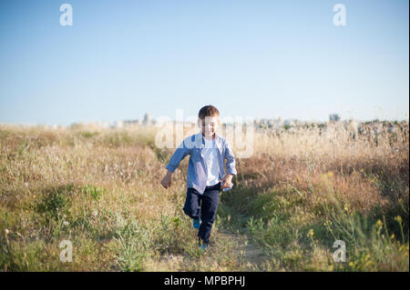 happy smiling little boy walking among yellow grass in summer sunny day Stock Photo