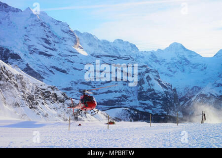 Maennlichen, Switzerland - December 31, 2013: Red helicopter flying near Swiss Alps mountains Maennlichen in winter, Switzerland Stock Photo