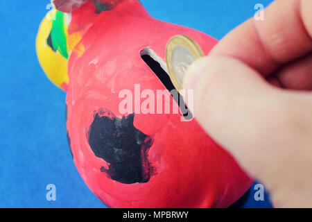 The hand drops the coin into the coin box. The concept of saving money. red piggy bank, painted by a child on a blue background Stock Photo