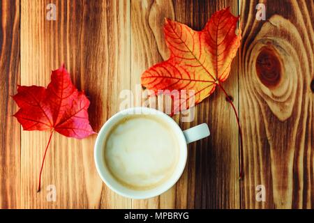 a cup of fragrant coffee and two autumn bright colored maple leaves on a wooden table. Top view Stock Photo