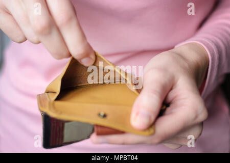 empty wallet in the hands of a young woman in a pink sweater. The concept of poverty, insolvency Stock Photo