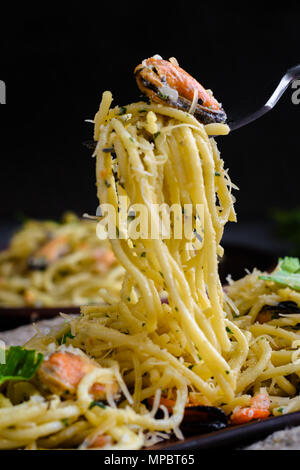 pasta with seafood in a creamy sauce wrapped on a fork rises from the plate. Italian cuisine, pasta with mussels and shrimps. Stock Photo