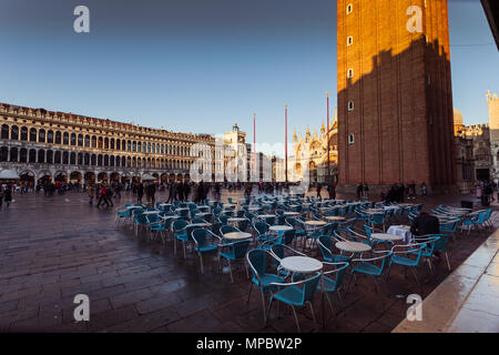 VENICE, ITALY - JANUARY 02 2018: Florian Cafe small tables in San Marco square with cathedral and bell tower shadow at evening time. Florian is an his Stock Photo