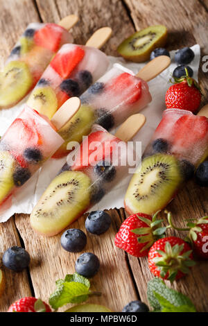 Freshly prepared popsicles ice with fresh strawberries, kiwi and blueberries on a stick close-up on a table. vertical Stock Photo