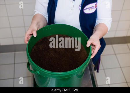 18 May 2018, Germany, Berlin: Melanie Potalivo, employee of the Technical University (TU) Berlin, holding a bucket with coffee grounds, which is collected at the canteen and kept for people to pick up themselves. The demand for fertiliser is increasing with the begin of the gardening season among Berlin's balcony gardeners and allotment holders. They are able to collect coffee grounds as fertiliser free of charge at Berlin universities. Photo: Kristin Bethge/dpa Stock Photo