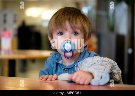 18 month old baby boy sat in high chair with dummy and comfort blanket Stock Photo