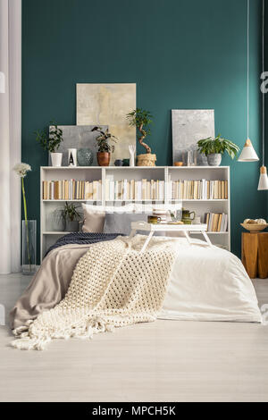 White breakfast tray on a cozy bed with warm blankets in a natural green apartment interior with home library Stock Photo