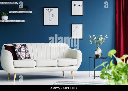 Leather sofa, floral paintings on the blue wall and flower in a vase in a living room interior Stock Photo
