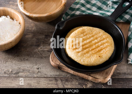 Arepas in frying pan on wooden table. Venezuelan typical food. Stock Photo