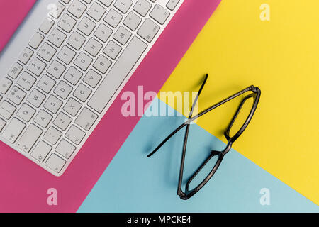 Computer keyboard eyeglasses on bright pink yellow background Stock Photo