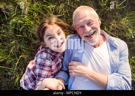 A small girl with grandfather outside in spring nature, relaxing on the grass. Stock Photo