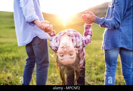 A small girl with her senior grandparents having fun outside in nature at sunset. Stock Photo