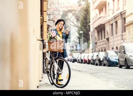 Young woman with bicycle and smartphone in sunny spring town. Stock Photo