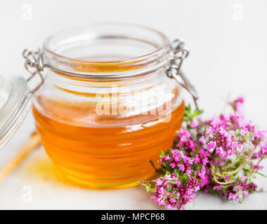 Raw organic thyme honey in a glass jar with thyme flowers herb Stock Photo