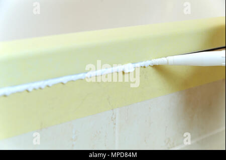 Worker puts silicone sealant to caulk the joint between tub and wall. Stock Photo