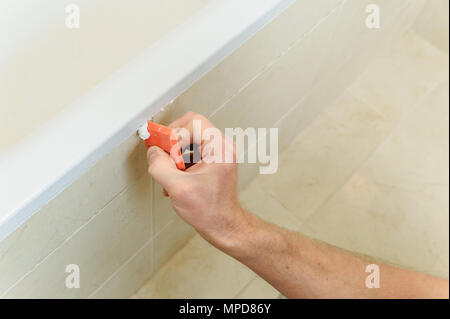 Worker smoothing silicone sealant between the bath and the wall using a spatula. Stock Photo