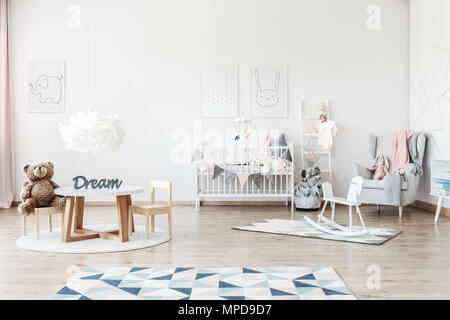 Plush bear toy on small chair at table in child's bedroom with toys and grey armchair