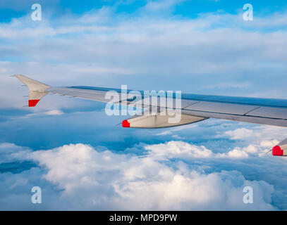 British Airways Airbus 319 plane wing seen from plane window during flight above puffy and wispy clouds and clear blue sky in United Kingdom Stock Photo