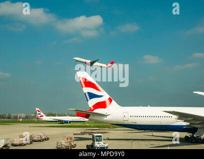 British Airways Boeing 777 on airport apron, Virgin Atlantic aeroplane taking off in blue sky, Terminal 5, Heathrow airport, London, England, UK Stock Photo