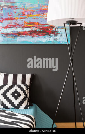 Close up of a bedroom with pattern bedding, floor lamp and modern picture on a black wall Stock Photo