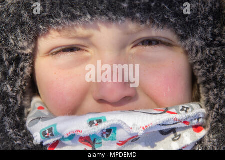 Boy's face with narrowed eyes in  hat and scarf in street close up Stock Photo