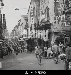 1950s, historical picture of a bustling city centre street in Hong Kong. Post-war, the territory, still a british colony, saw rapid economic growth, fuelled by a vast increase in population - by the mid fifties Hong Kong's population density was one of the highest in the world - and a relocation of businesses and resources from communist China. Stock Photo