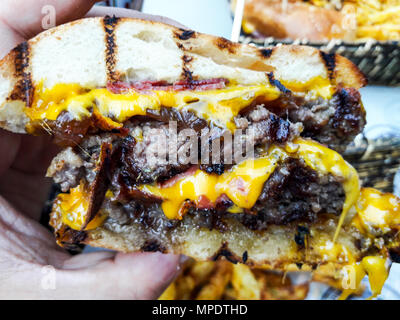 Holding Hamburger with melted cheddar cheese. Fast Food Concept. Stock Photo