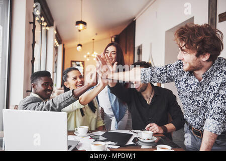 Happy young entrepreneurs in casual clothes at cafe table or in business office giving high fives to each other as if celebrating success or starting new project Stock Photo