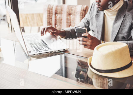 Pensive afro american handsome professional writer of popular articles in blog dressed in trendy outfit and glasses thinking over new story proofreading his script from notebook sitting in cafe Stock Photo