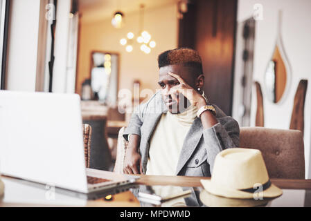 Pensive afro american handsome professional writer of popular articles in blog dressed in trendy outfit and glasses thinking over new story proofreading his script from notebook sitting in cafe Stock Photo