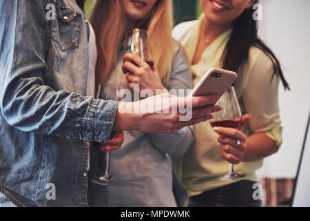 Picture presenting a happy group of girl friends with red wine. Together they see a photo on a smartphone
