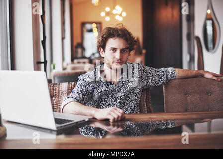 Young handsome man sitting in office with cup of coffee and working on project connected with modern cyber technologies. Businessman with notebook trying to keep deadline in digital marketing sphere Stock Photo