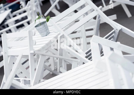 Heaps of inverted white plastic chairs on tables in closed restaurant on terrace close-up. Beautiful graphic chaos, interesting background Stock Photo