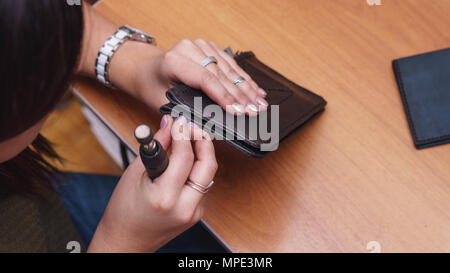Tanner grinds edges of leather purse. Handmade. Workflow in workshop. Shooting close-up. Stock Photo