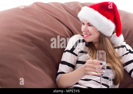 Cheerful girl in the Santa Claus hat. Girl sitting on a chair with a glass of champagne. Stock Photo