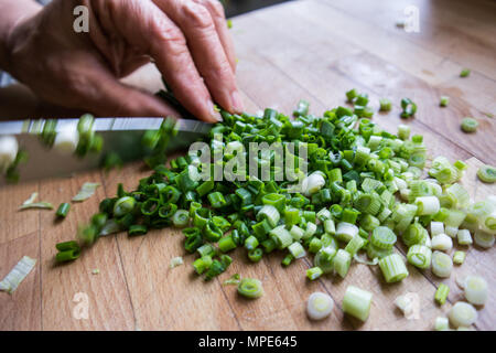 Woman chopping green onions with knife on wooden surface. Stock Photo