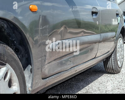 Close up detail of a dented driver door from a car crash or automobile accident. Bent and distorted metal with large dent and body paint scratched Stock Photo