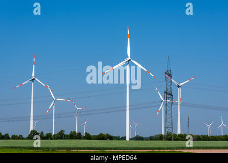 Overhead power lines and wind power plants under a blue sky in Germany Stock Photo