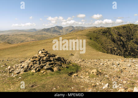Cairn next to a stoney footpath in the Lake District, UK. The path leads into the distance with the Crinkle Crags in the background under a cloudy sky Stock Photo