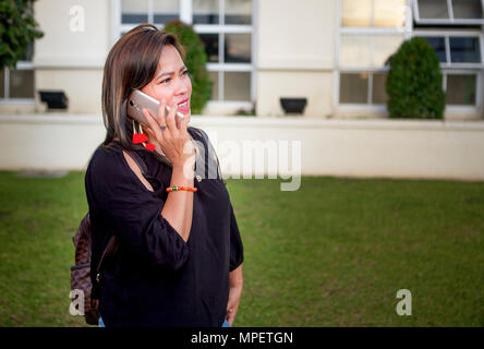 Portrait of a young, Asian businesswoman talking on a smartphone outside an office building in the Philippines. Stock Photo