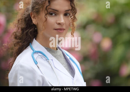 Portrait of a young woman, doctor, physician, medical practitioner in lab coat in natural outdoor settings