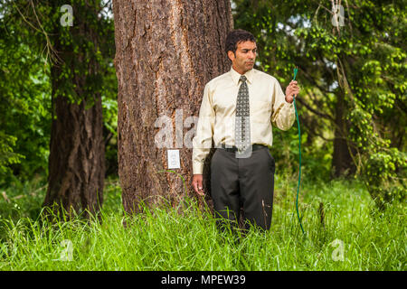 Conceptual shot of a businessman holding a green extension cord with an electrical outlet in the tree next to him. Illustrating green power. Stock Photo