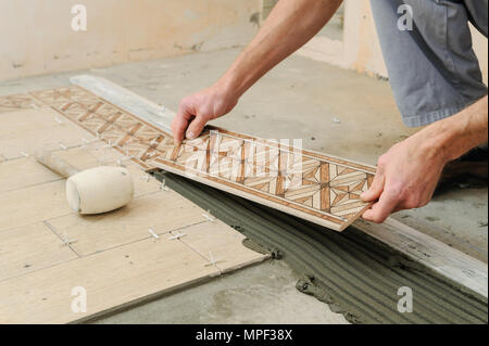 Worker putting tiles on the floor. It installs strips. Stock Photo