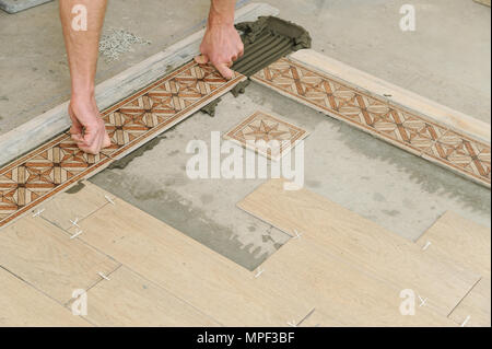 Worker putting tiles on the floor. It installs strips. Stock Photo