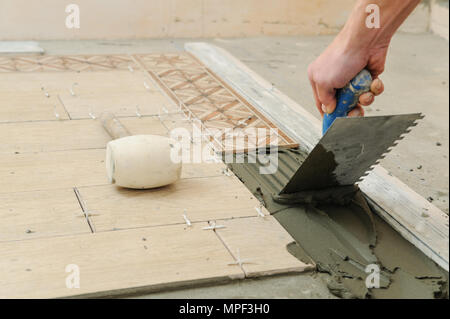 Worker instalis tiles on the floor. He put glue using comb trowel. Stock Photo