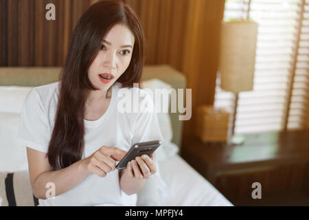 Shocked young woman using mobile phone on a bed Stock Photo