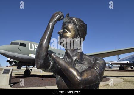 'Rosie the Riveter' rolls up her sleeve in this bronze bust symbolizing the contributions to the war-effort made during and after World-War II by women in the Charles B. Hall Memorial Air Park on Feb. 16, 2017, at Tinker Air Force Base, Oklahoma. Many women worked in the Douglas Aircraft manufacturing plant in Oklahoma City to produce C-47 aircraft like the one visible behind her. The free public park features aircraft operated or maintained by Tinker AFB over the years and is located near the main entrance to the base with free parking available. (U.S. Air Force photo/Greg L. Davis) Stock Photo