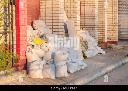 construction waste in white construction bags lie on the street near the brick wall. Stock Photo