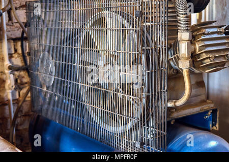 Electrical air compressor with a large fan in front panel behind a metal protective mesh Stock Photo